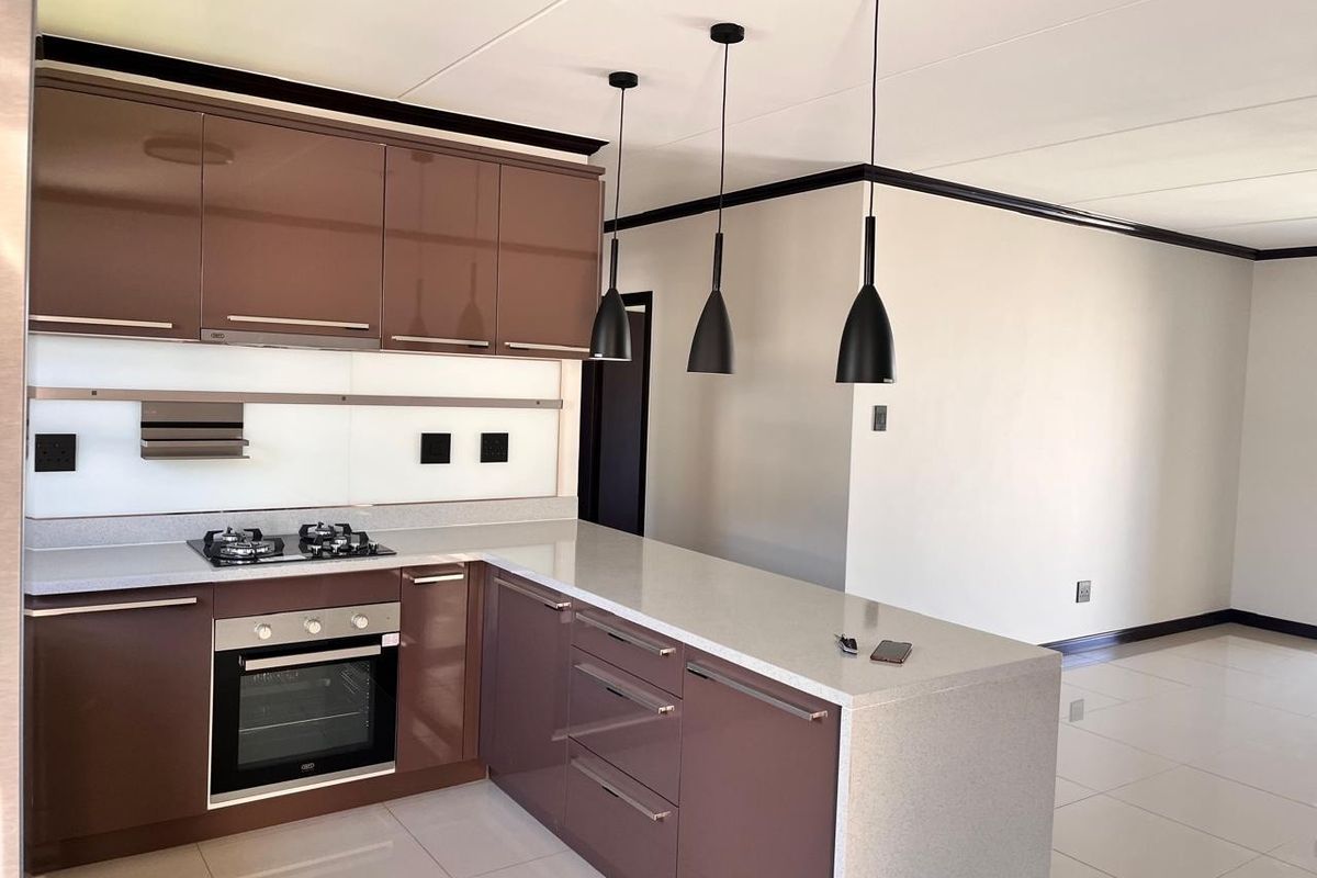 Modern open-plan kitchen featuring high-gloss brown cabinetry, stone countertops, integrated gas hob, built-in oven, and stylish pendant lighting over a functional island.
