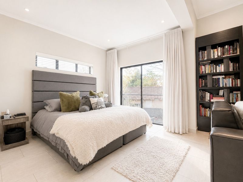 A bright and modern bedroom featuring tiled flooring, recessed lighting, a built-in bookshelf, and a sliding glass door leading to an outdoor area.
