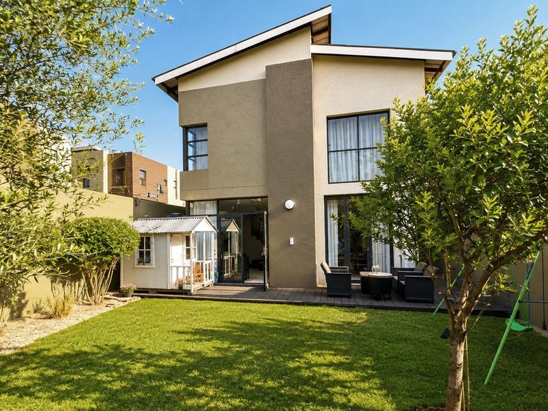 Rear view of a modern two-story house featuring a timber deck, landscaped garden, and large sliding glass doors providing seamless indoor-outdoor flow.