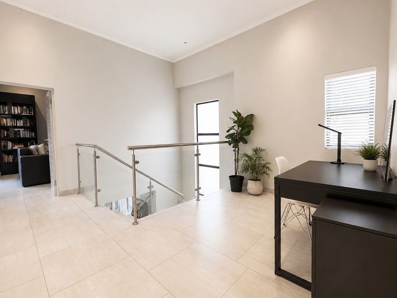 A bright and modern landing area featuring tiled flooring, a sleek glass balustrade with stainless steel handrails, and neutral wall finishes.