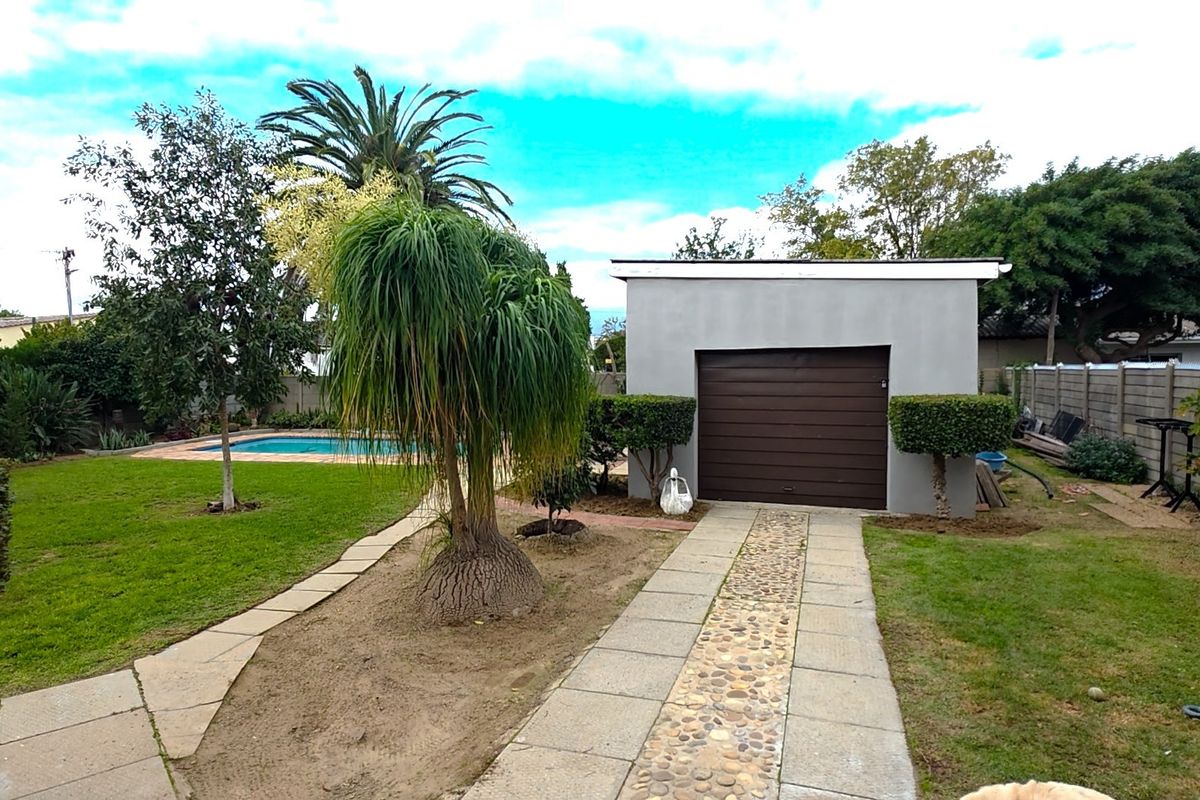 Rear garden view featuring a swimming pool, a detached garage with a roller door, and a paved walkway leading through the lawn.
