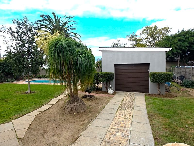 Rear garden view featuring a swimming pool, a detached garage with a roller door, and a paved walkway leading through the lawn.