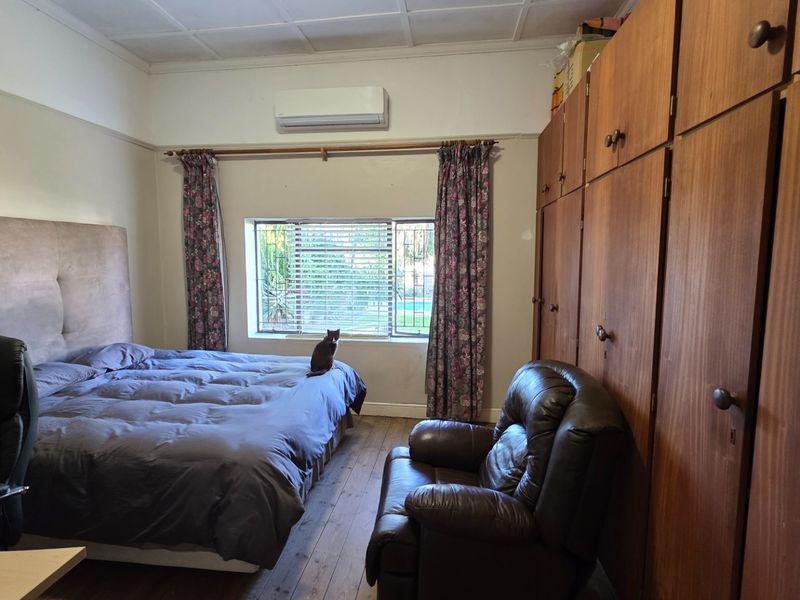 A bedroom featuring timber flooring, extensive built-in wooden cupboards, and a wall-mounted air conditioning unit.