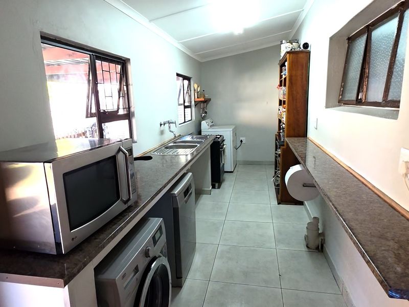A functional scullery area featuring tiled flooring, laminate countertops, a stainless steel sink, and dedicated space for laundry appliances.