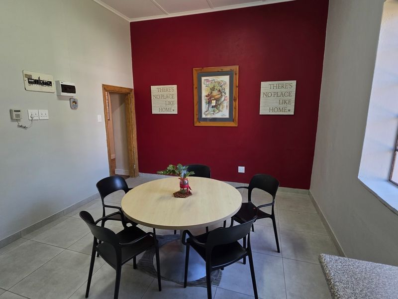 A dining area featuring tiled flooring and a large steel-framed window, accented by a bold red feature wall.
