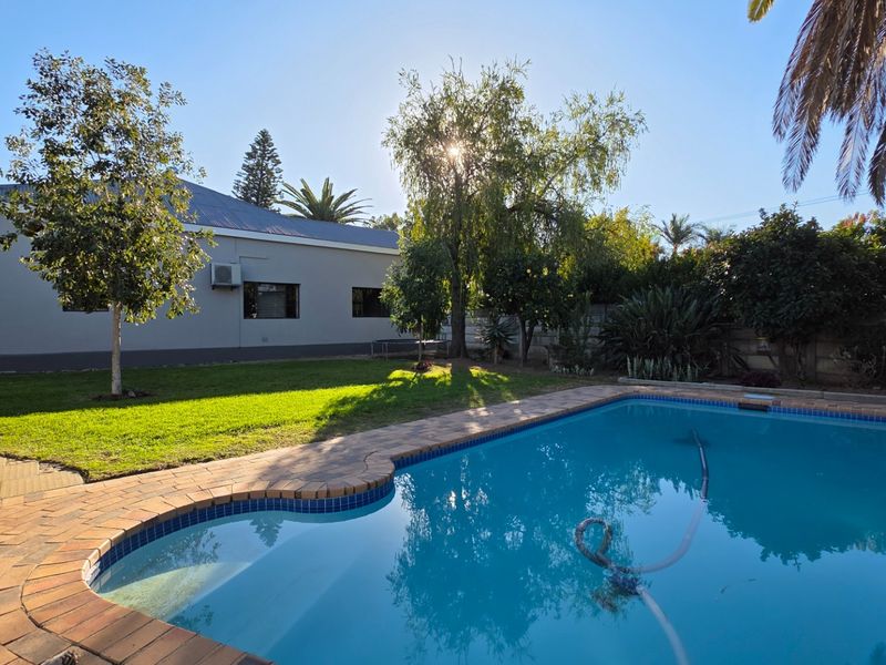 A well-maintained backyard featuring a swimming pool with brick coping, a manicured lawn, and established garden trees.
