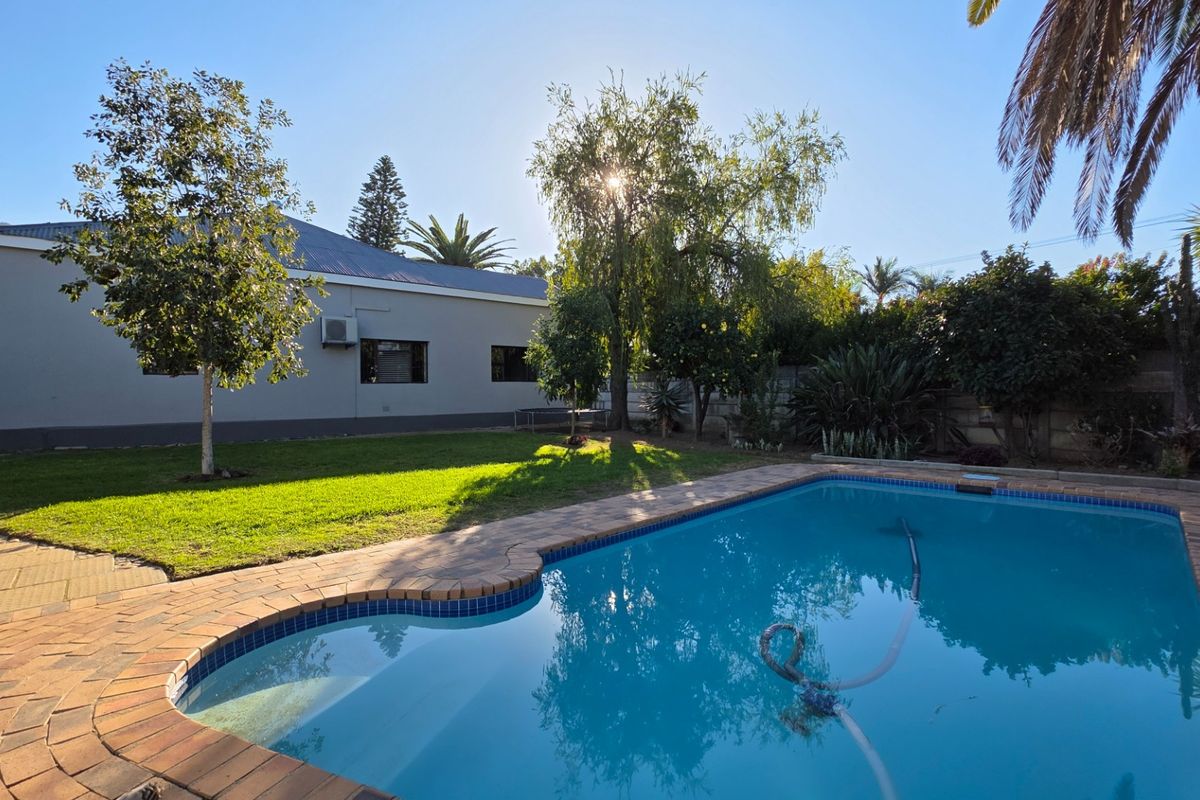 A well-maintained backyard featuring a swimming pool with brick coping, a manicured lawn, and established garden trees.
