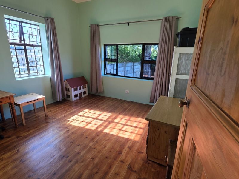 A bedroom featuring warm timber flooring, natural light from dual windows with security bars, and neutral wall finishes.