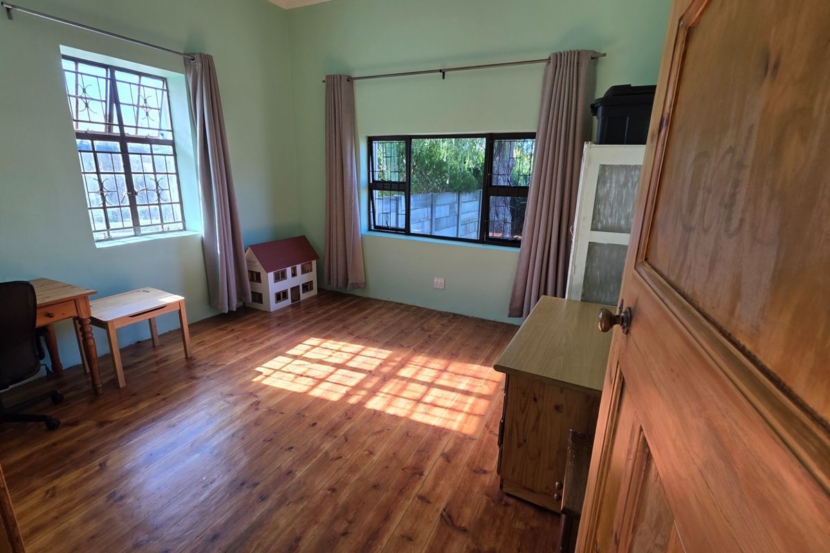 A bedroom featuring warm timber flooring, natural light from dual windows with security bars, and neutral wall finishes.