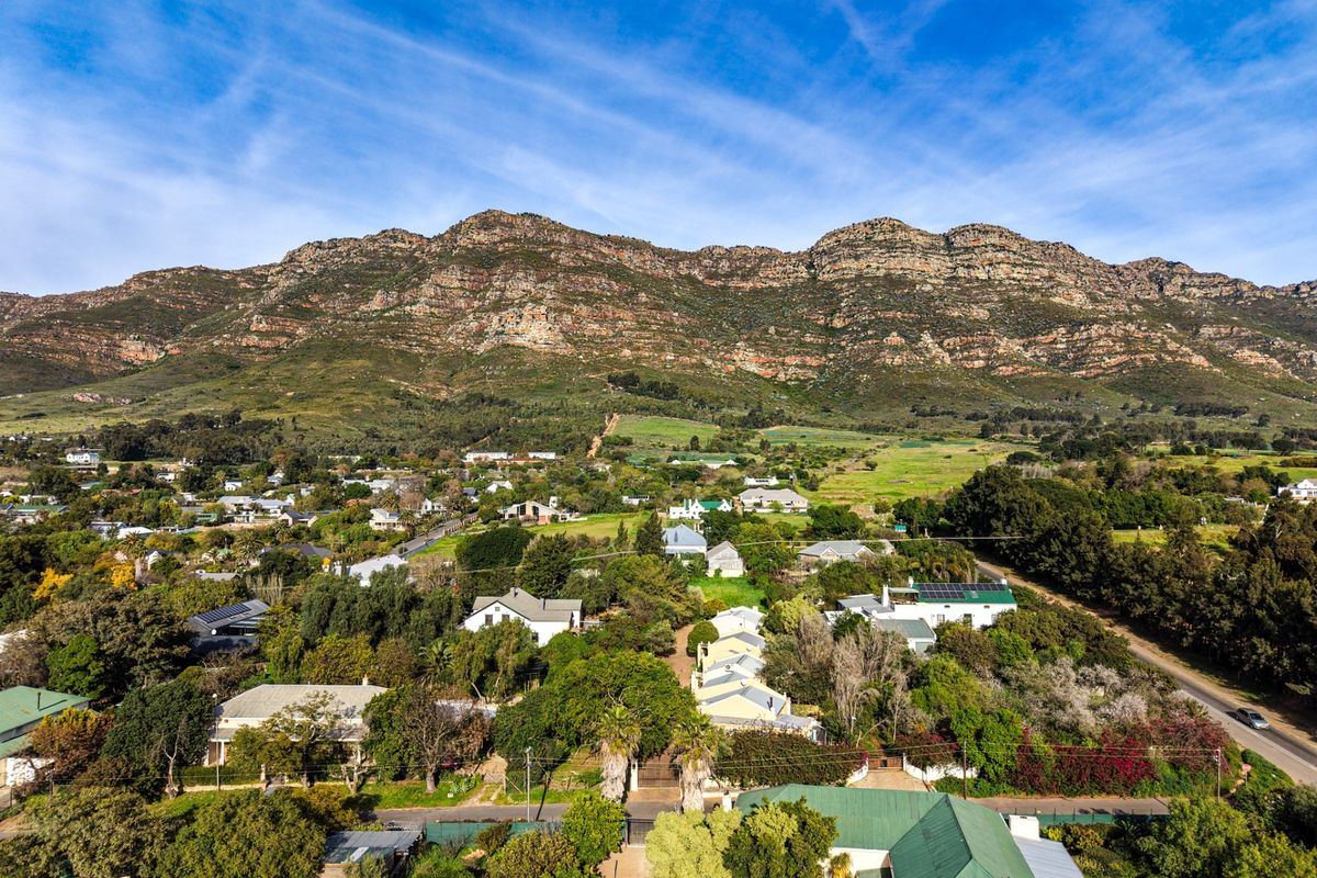 An elevated aerial view showcasing the property's location within a lush, green residential neighborhood set against a dramatic mountain backdrop.
