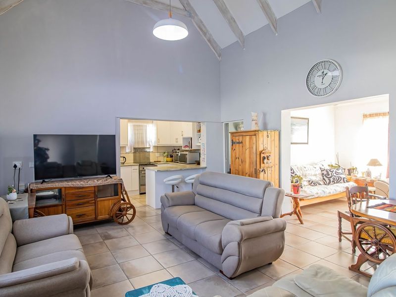 Spacious open-plan living area featuring vaulted ceilings with exposed rafters, tiled flooring, and a connected kitchen with island seating.