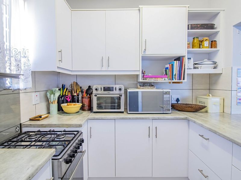 A functional kitchen featuring white cabinetry, laminate countertops, a gas stove, and a tiled backsplash, offering a clean and practical workspace.