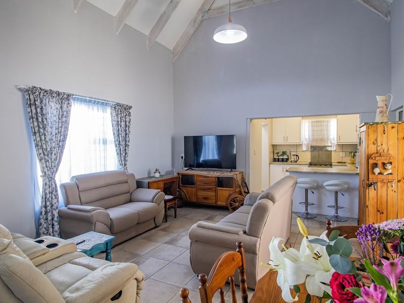 Spacious open-plan living area featuring a high vaulted ceiling with exposed beams, tiled flooring, and a functional kitchen with a breakfast bar.