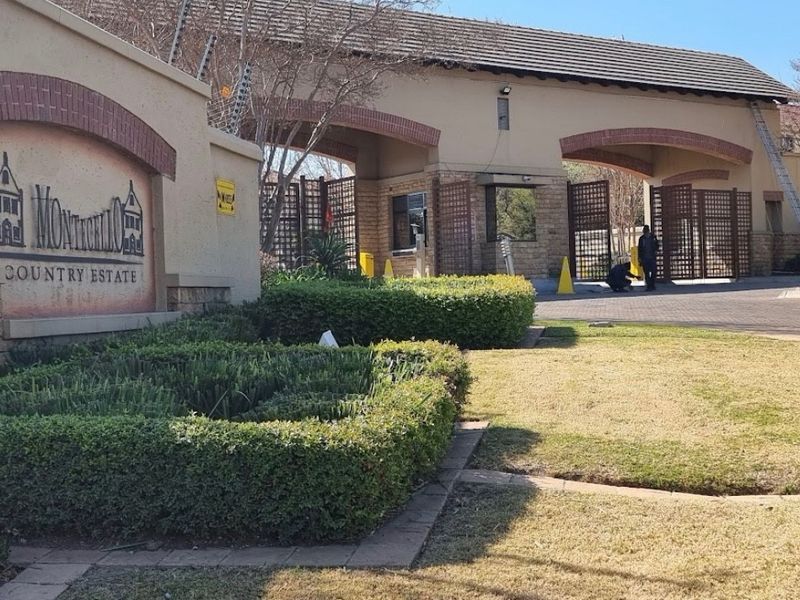 The entrance to Monticello Country Estate featuring a secure gatehouse, paved driveway, and well-maintained landscaped hedging.