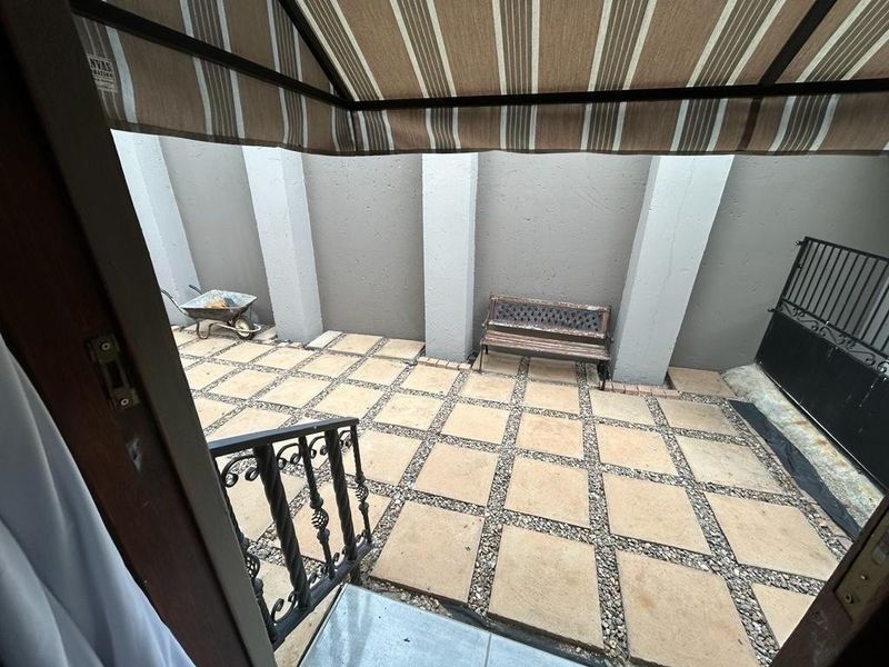 A paved outdoor patio area featuring a retractable awning, wrought iron railings, and high boundary walls for privacy.