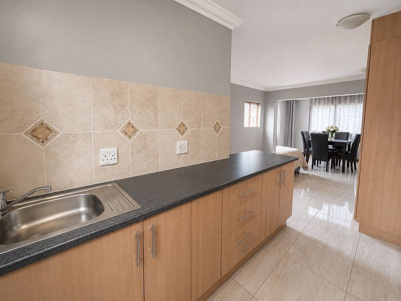 Open plan kitchen area featuring laminate cabinetry, dark countertops, and tiled flooring, seamlessly flowing into the adjacent dining space.