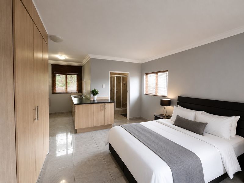 A spacious bedroom featuring built-in cupboards, tiled flooring, and an integrated kitchenette area with an en-suite bathroom.