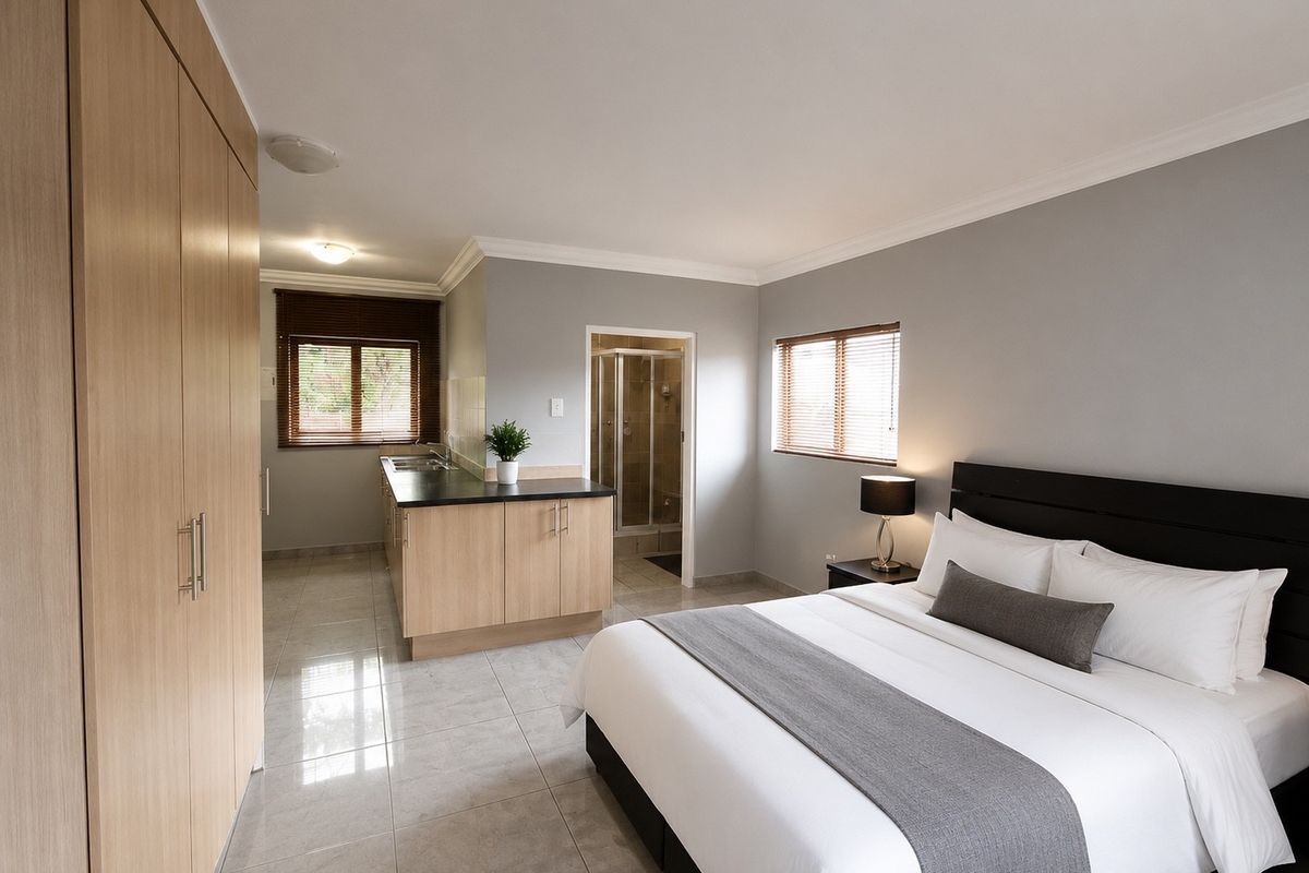 A spacious bedroom featuring built-in cupboards, tiled flooring, and an integrated kitchenette area with an en-suite bathroom.