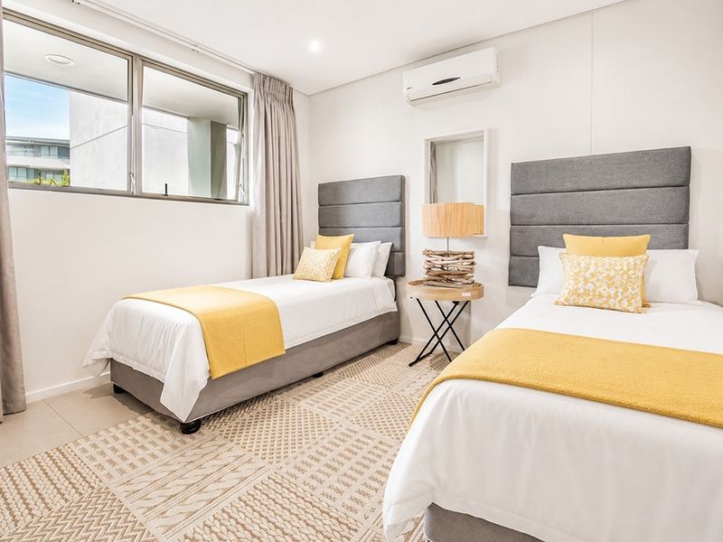 A bright and modern bedroom featuring neutral tones, a split-system air conditioner, and large windows allowing for ample natural light.