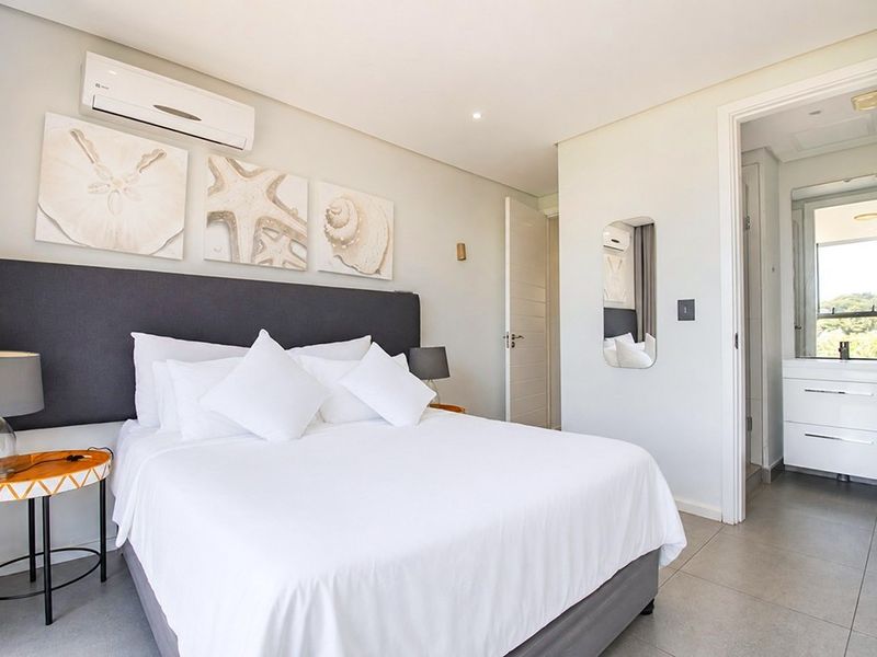 A well-maintained bedroom featuring tiled flooring, a split-system air conditioner, and an adjoining en-suite bathroom with modern vanity.