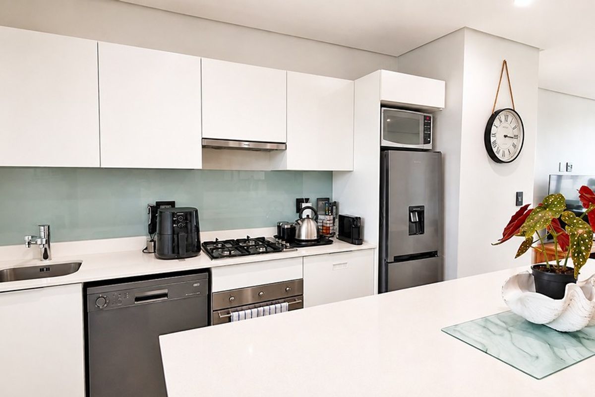 Modern kitchen featuring sleek white cabinetry, stone countertops, a glass splashback, and high-quality built-in appliances including a gas hob and oven.