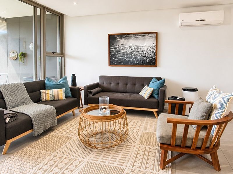 A bright and modern living room featuring large sliding glass doors, tiled flooring, and a wall-mounted split-system air conditioner.