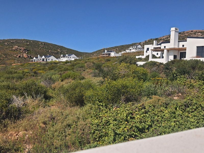 A scenic view of the residential estate landscape featuring natural coastal vegetation and surrounding hillside properties.