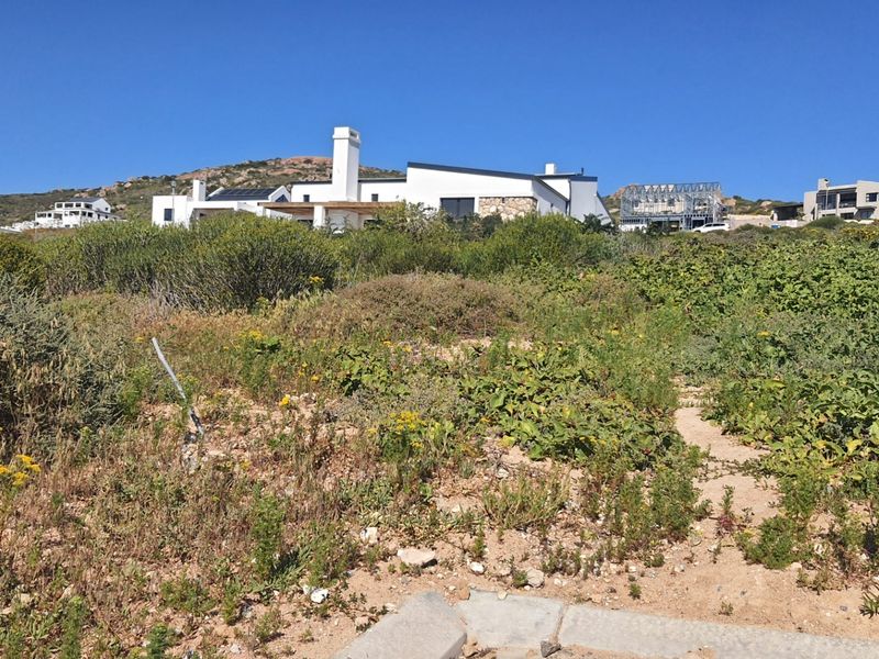 A view of a vacant residential plot featuring natural coastal vegetation with surrounding residential properties in the background.