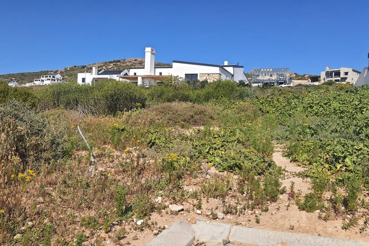 A view of a vacant residential plot featuring natural coastal vegetation with surrounding residential properties in the background.