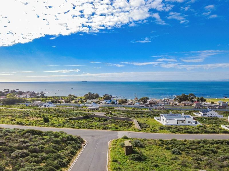 An aerial view of a vacant residential plot situated in a coastal neighborhood with clear ocean views and established road access.
