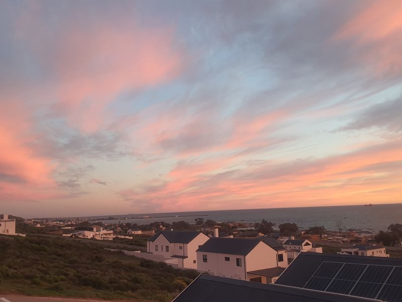 A scenic coastal view overlooking the residential neighborhood and ocean at sunset, featuring visible solar panel installations on nearby rooftops.