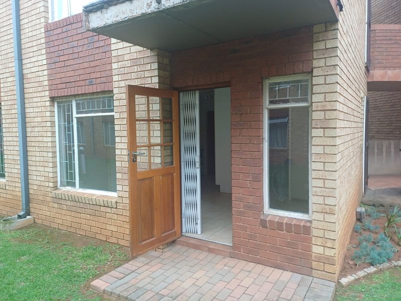 Exterior view of an apartment entrance featuring a brick facade, timber door, and security gate with a paved entryway.