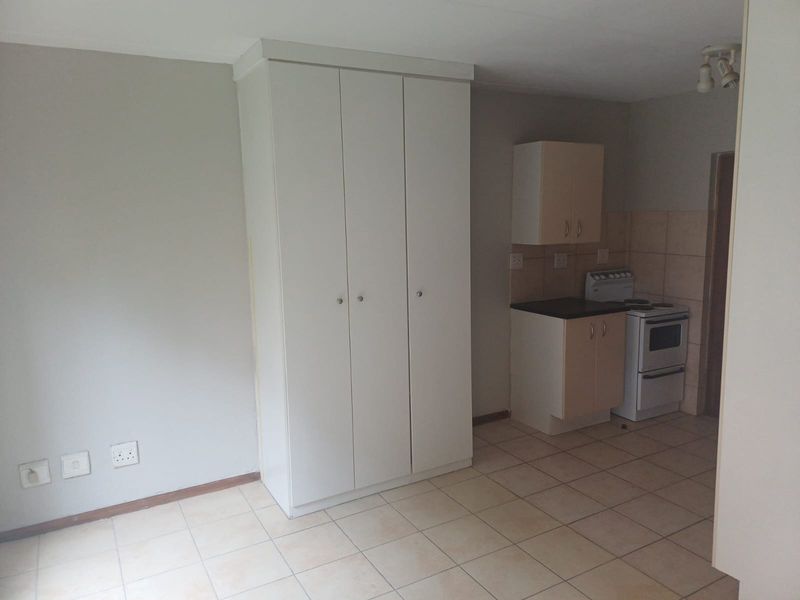 An open-plan living area featuring tiled flooring, built-in storage cupboards, and a compact kitchen space equipped with cabinetry and a freestanding stove.
