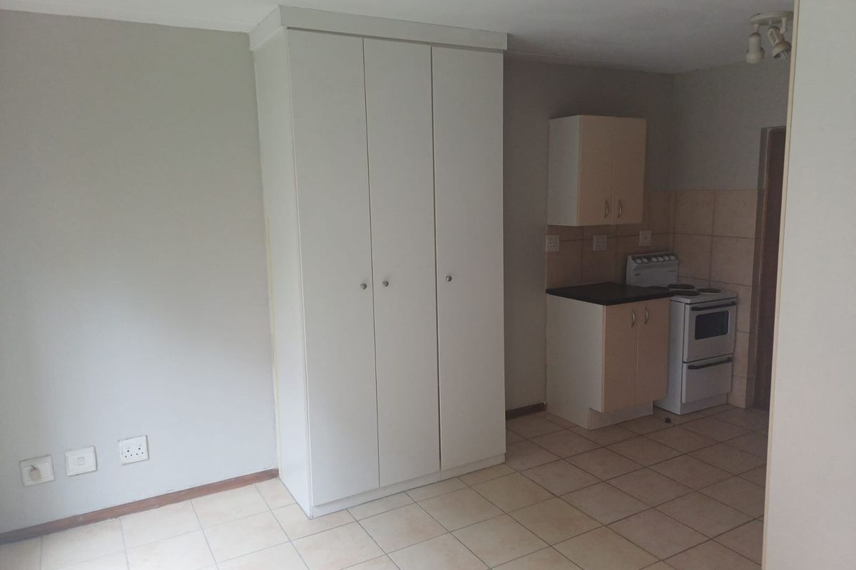 An open-plan living area featuring tiled flooring, built-in storage cupboards, and a compact kitchen space equipped with cabinetry and a freestanding stove.