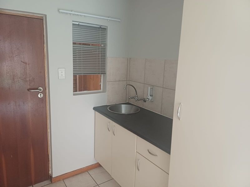 A compact scullery or utility area featuring built-in cabinetry, a stainless steel sink, tiled splashback, and tiled flooring.