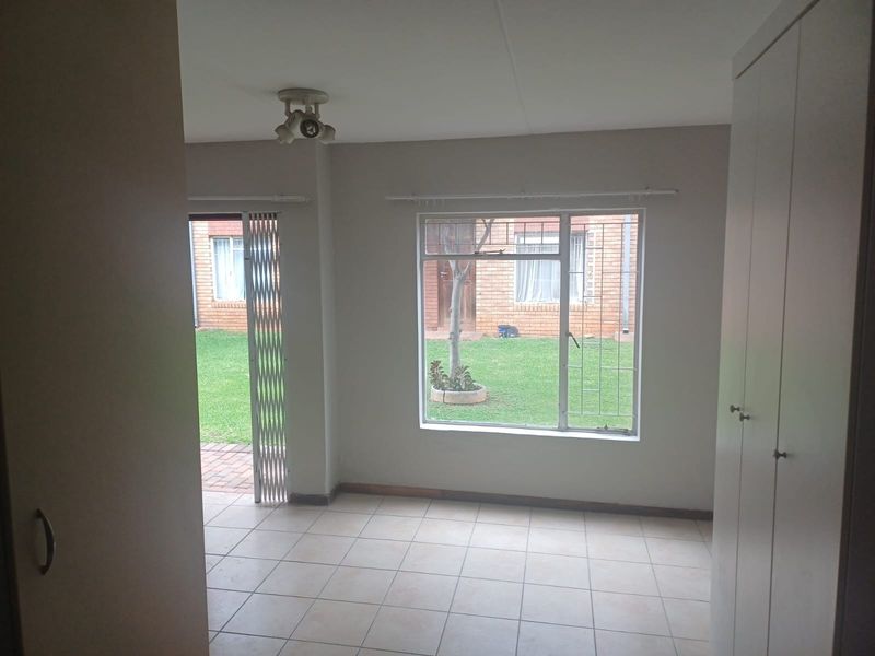 A bright, empty bedroom featuring tiled flooring, built-in cupboards, and direct access to a garden area through a security gate.