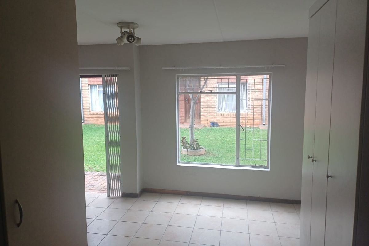 A bright, empty bedroom featuring tiled flooring, built-in cupboards, and direct access to a garden area through a security gate.