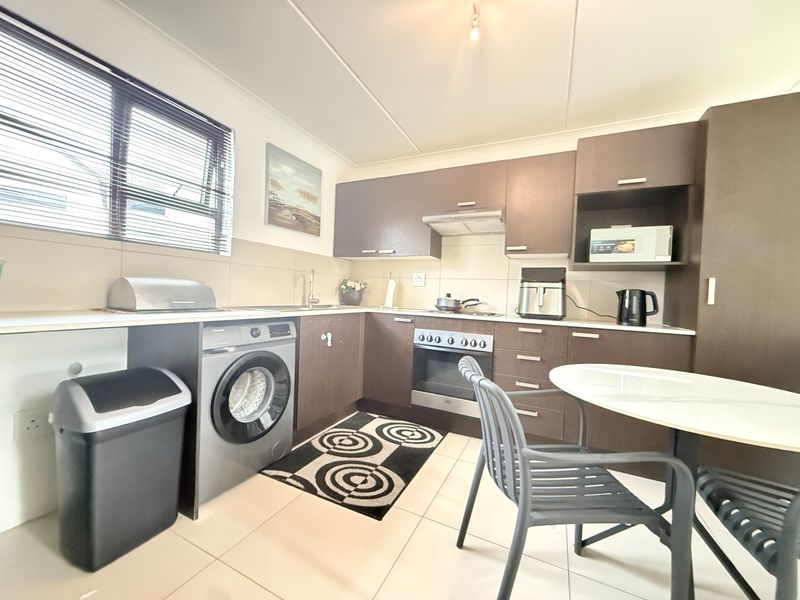 A functional kitchen featuring dark wood-finish cabinetry, built-in oven with extractor fan, tiled flooring, and a tiled backsplash with ample counter space.