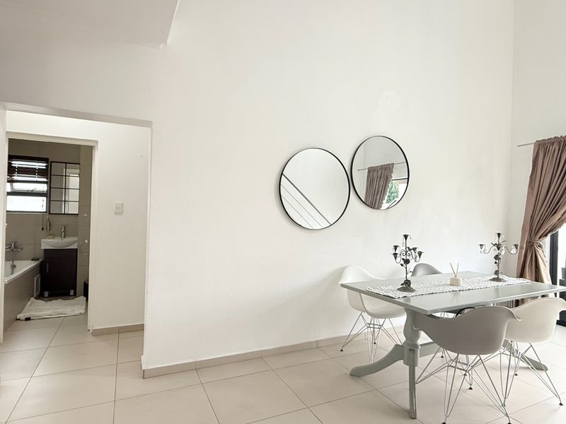An open-plan living and dining area featuring neutral tiled flooring, leading into an adjacent bathroom space.