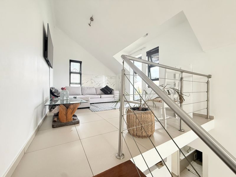 A bright, open-plan living area featuring modern tiled flooring, a sleek stainless steel balustrade, and a distinctive sloped ceiling with marble-look wall accents.