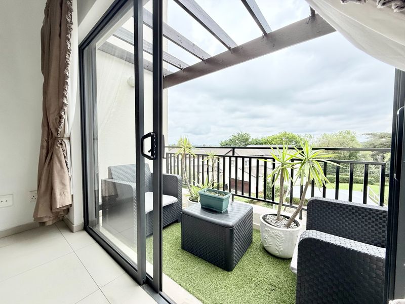 A covered balcony featuring a timber pergola, metal balustrade, and sliding glass door access, offering an outdoor space with tiled flooring.