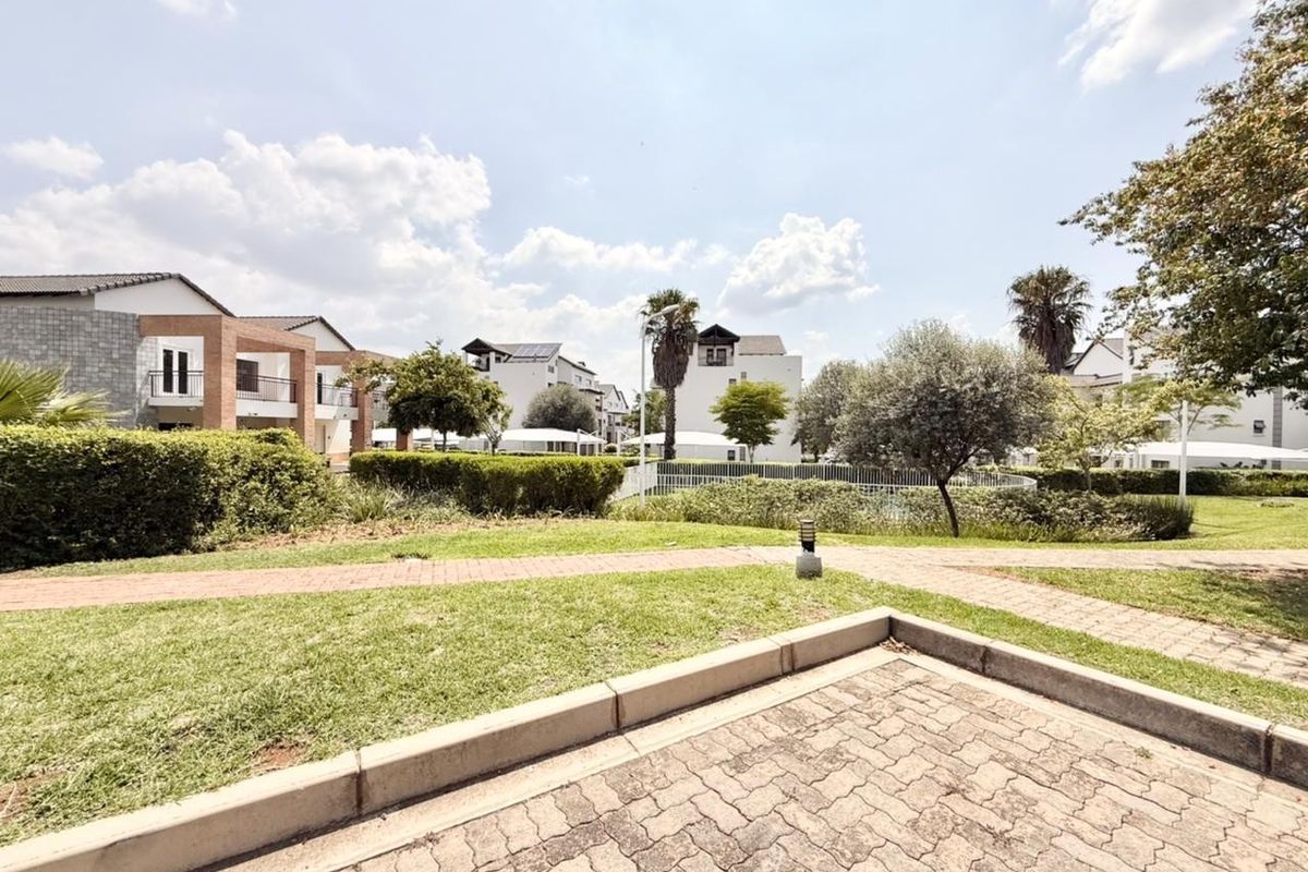A well-maintained communal garden area featuring paved walkways, manicured lawns, and established landscaping within a residential apartment complex.