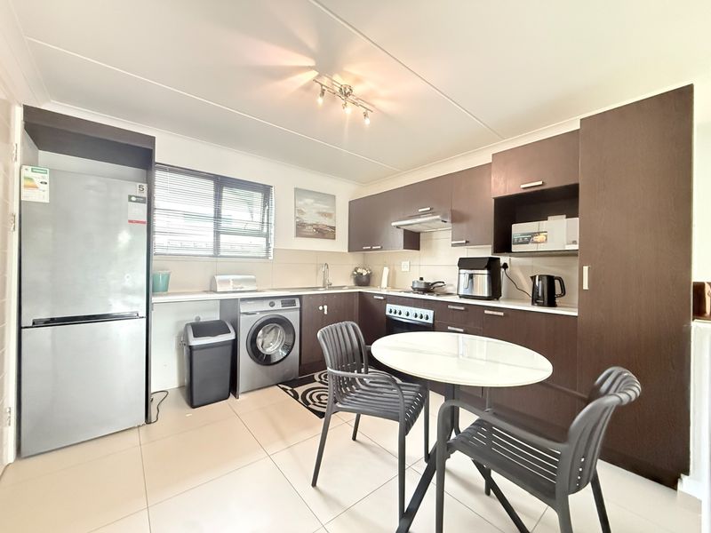 A functional kitchen featuring dark wood cabinetry, tiled flooring, integrated appliances, and a dedicated space for a washing machine.