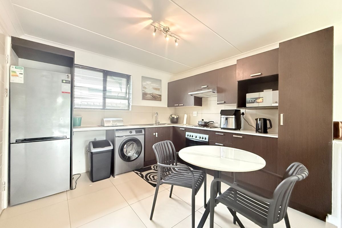 A functional kitchen featuring dark wood cabinetry, tiled flooring, integrated appliances, and a dedicated space for a washing machine.