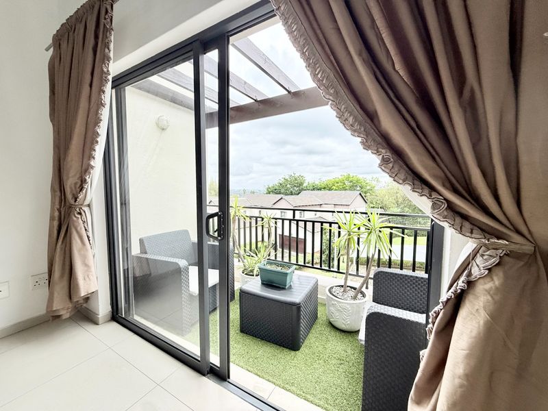 A covered balcony featuring a pergola, metal railing, and artificial grass flooring, offering an outdoor space accessible through sliding glass doors.