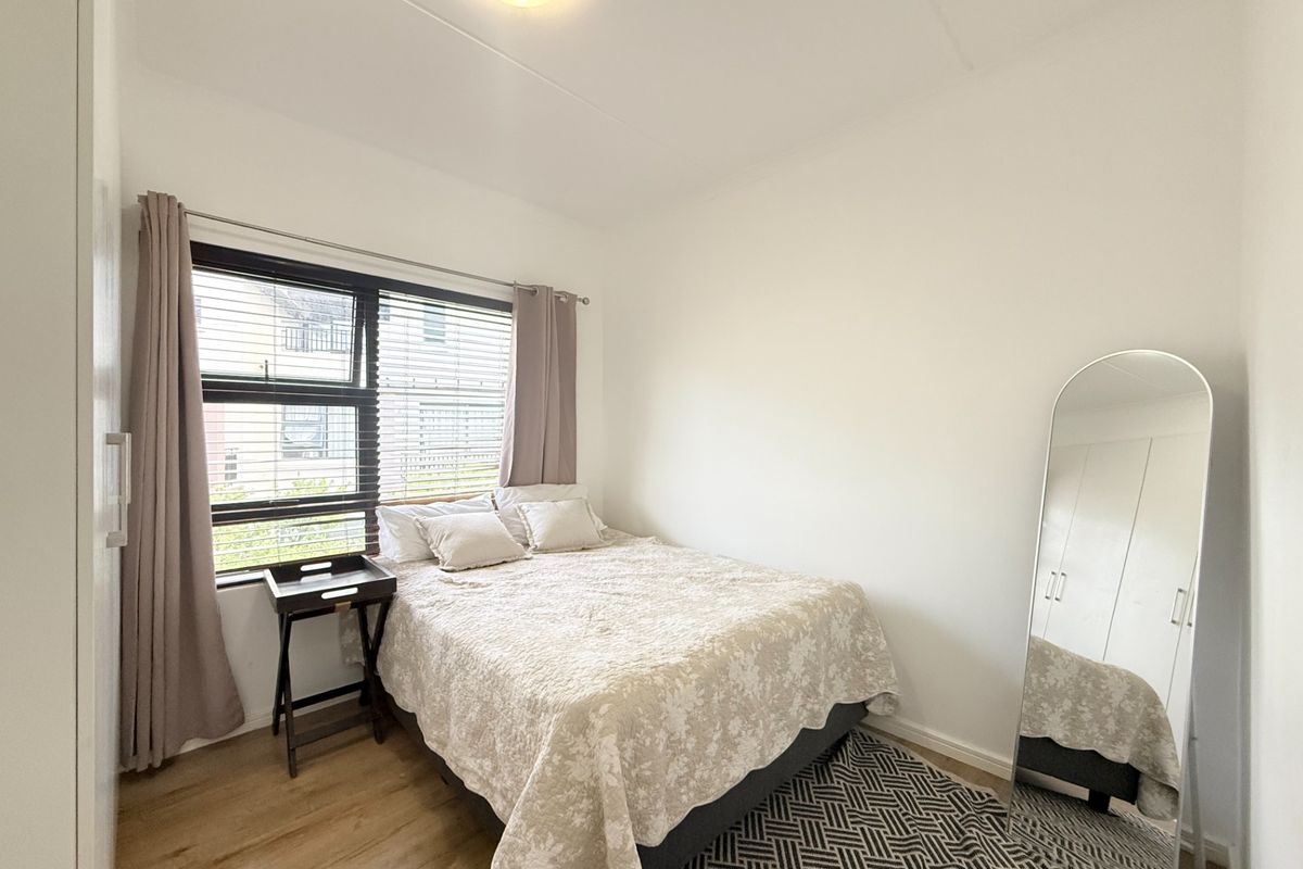 A well-maintained bedroom featuring laminate flooring, a built-in wardrobe, and an aluminium-framed window providing natural light.