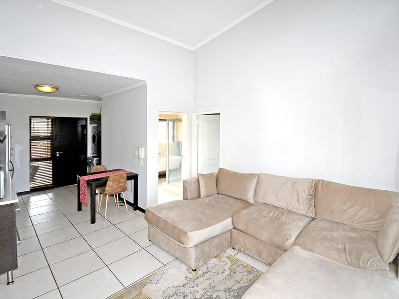 Open-plan living area featuring tiled flooring, a compact kitchen with built-in appliances, and direct access to adjacent rooms.
