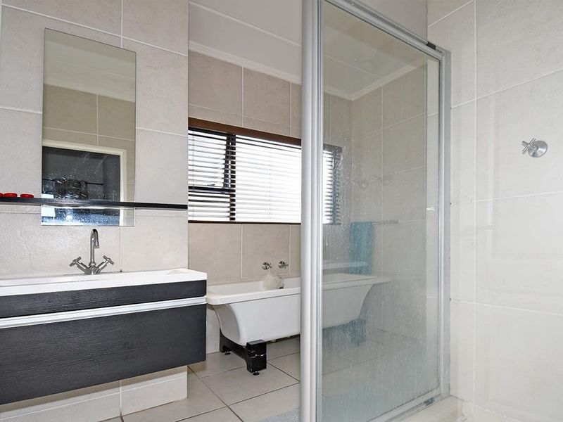 A functional bathroom featuring a freestanding bathtub, a modern vanity cabinet, and a separate glass-enclosed shower with neutral wall and floor tiling.