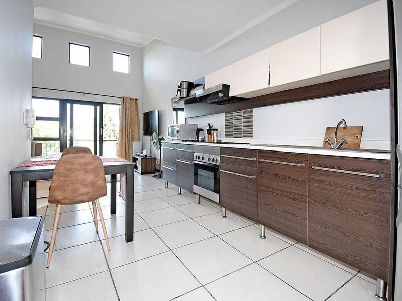 Open-plan kitchen and living area featuring modern two-tone cabinetry, built-in oven, tiled flooring, and access to a balcony through sliding glass doors.