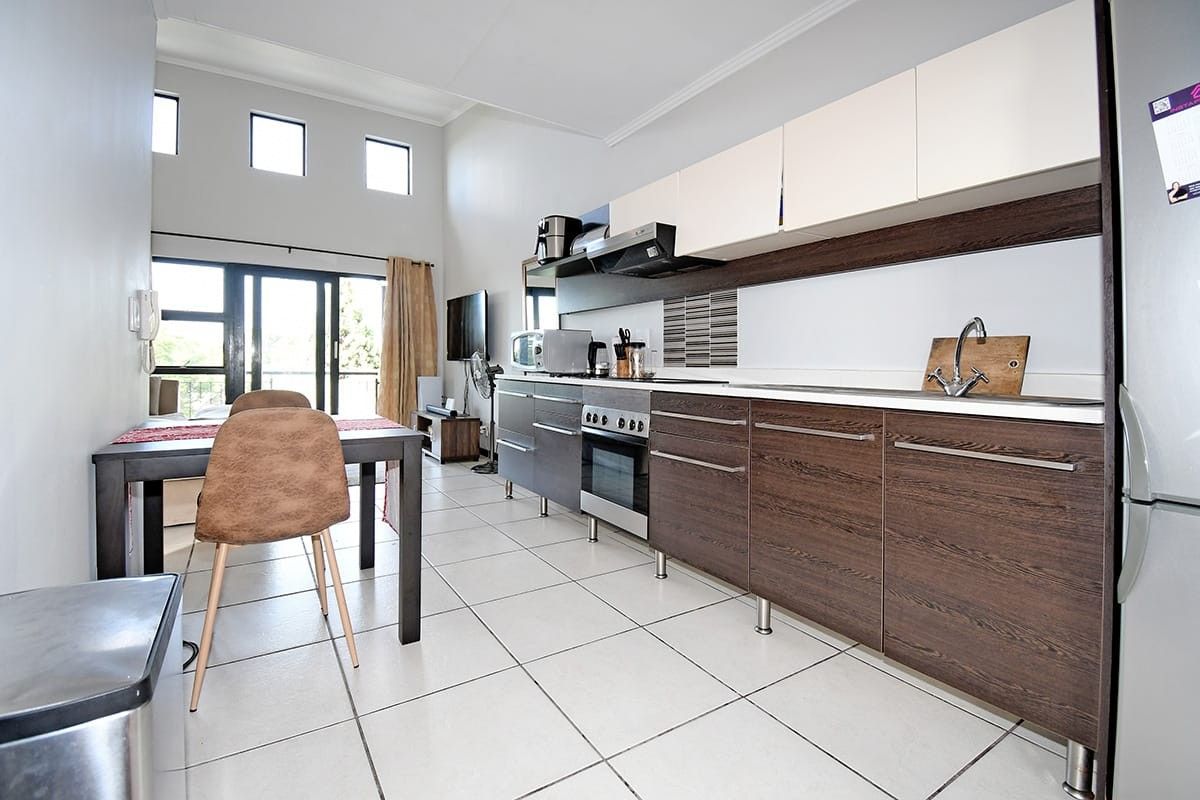 Open-plan kitchen and living area featuring modern two-tone cabinetry, built-in oven, tiled flooring, and access to a balcony through sliding glass doors.